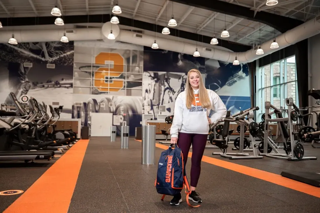 Student holds backpack in gym.